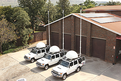 Four white monitoring vehicles equipped with antennas parked outside a brick building, representing LS telcom’s mobile spectrum monitoring solutions for flexible deployment.